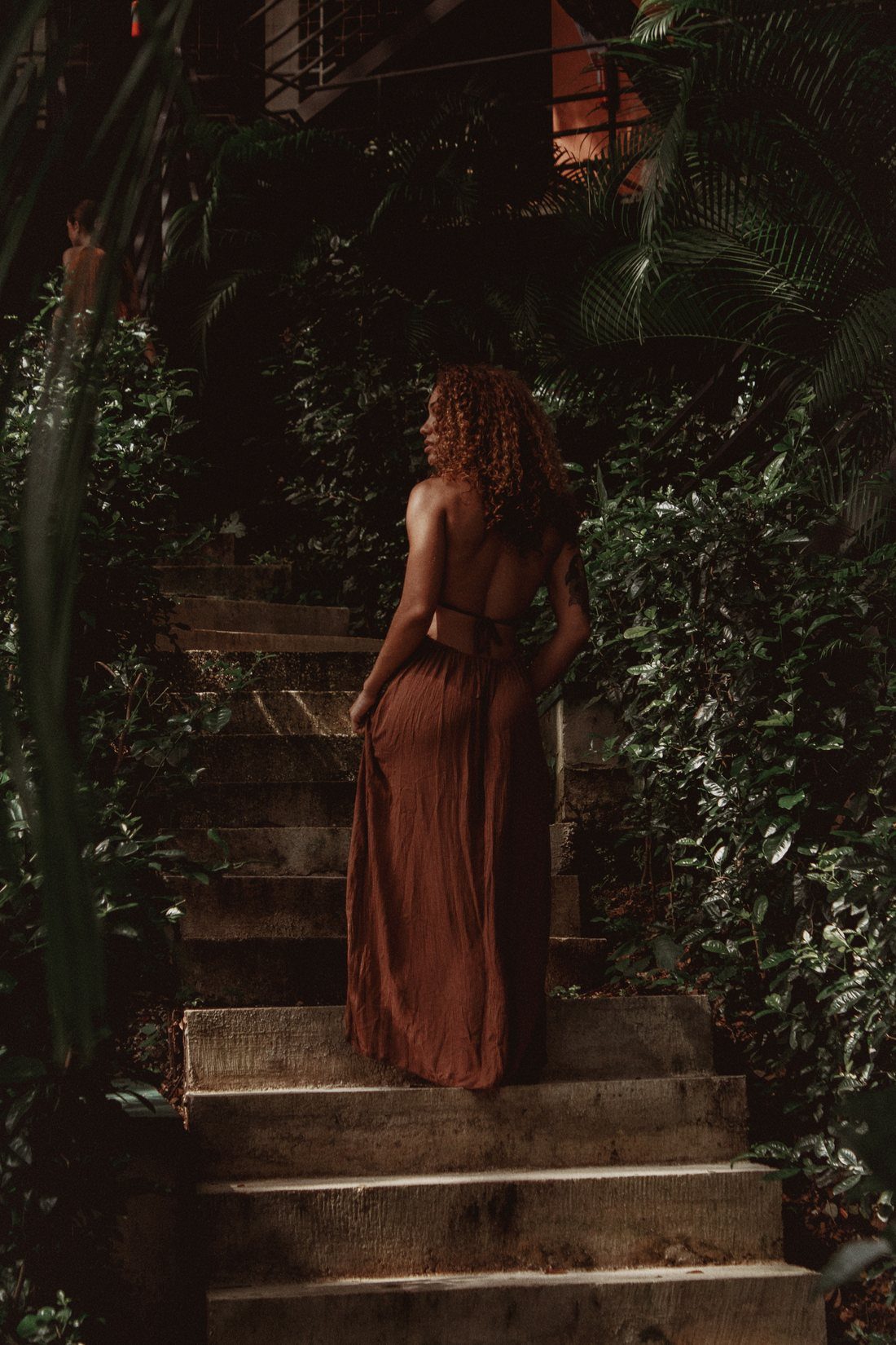 A guest in a flowing terracotta dress on the jungle stone stairway at Armonia in warm evening light