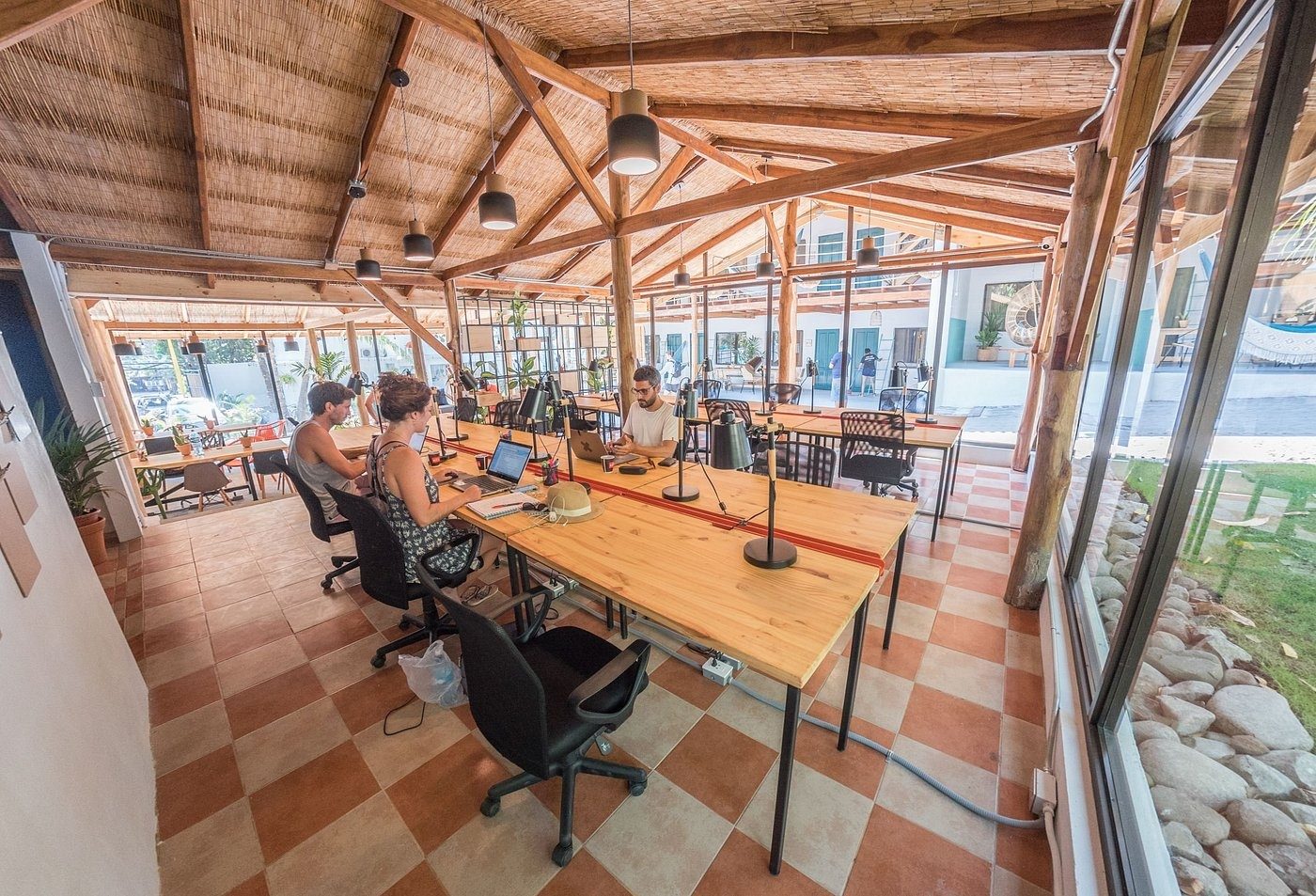 People working at long wooden desks with task lamps under a timber-beam roof