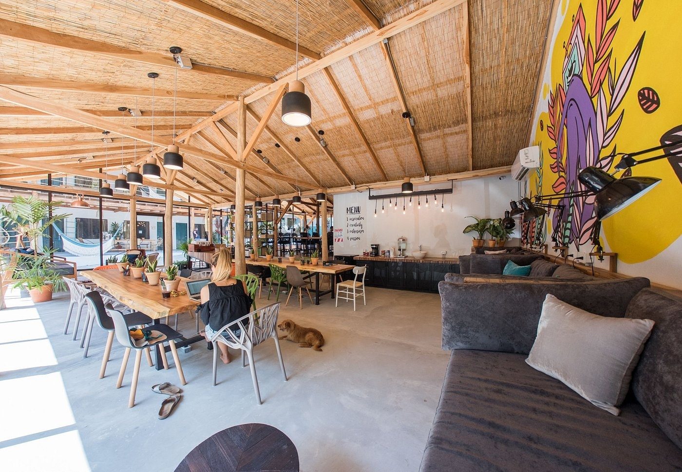 The wide open-air co-working hall at Armonia under a timber and thatch roof, with long desks and lounge seating
