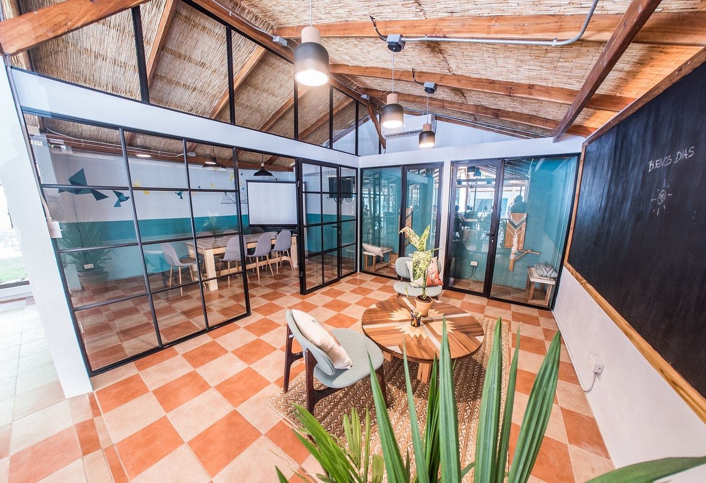Glass-walled meeting rooms and call booths under a thatch ceiling with terracotta floors