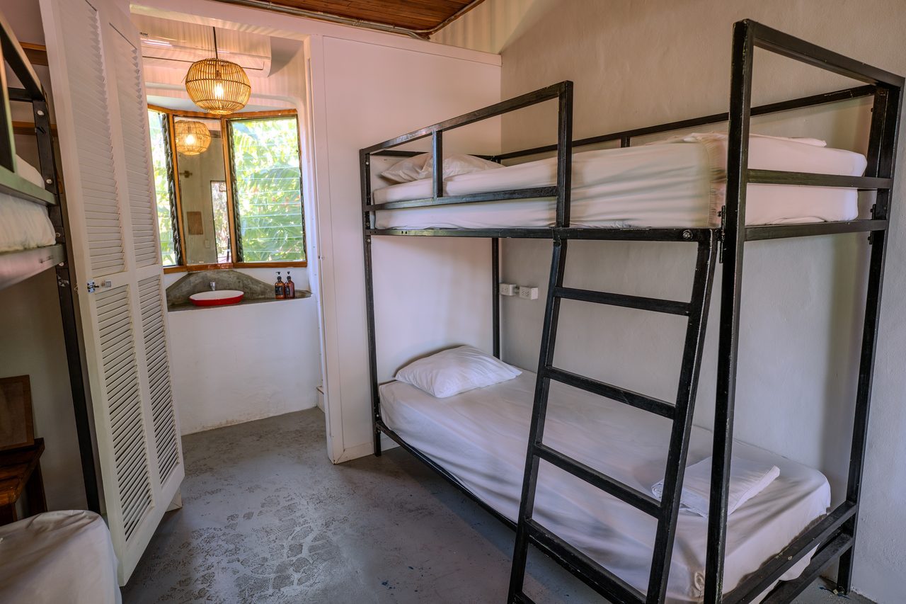 A four-bed dorm with steel bunks and its own in-room sink and bathroom by the window
