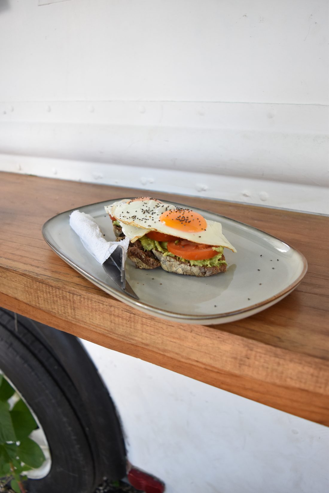 Avocado toast topped with a fried egg, tomato and chia seeds on a ceramic plate