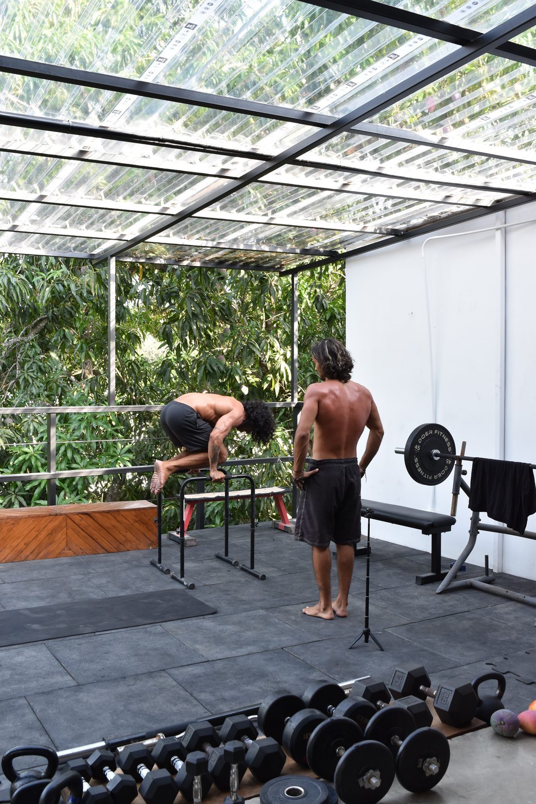 Pull-up and dip bars, a weight bench with plates and a full dumbbell rack in the open-air gym