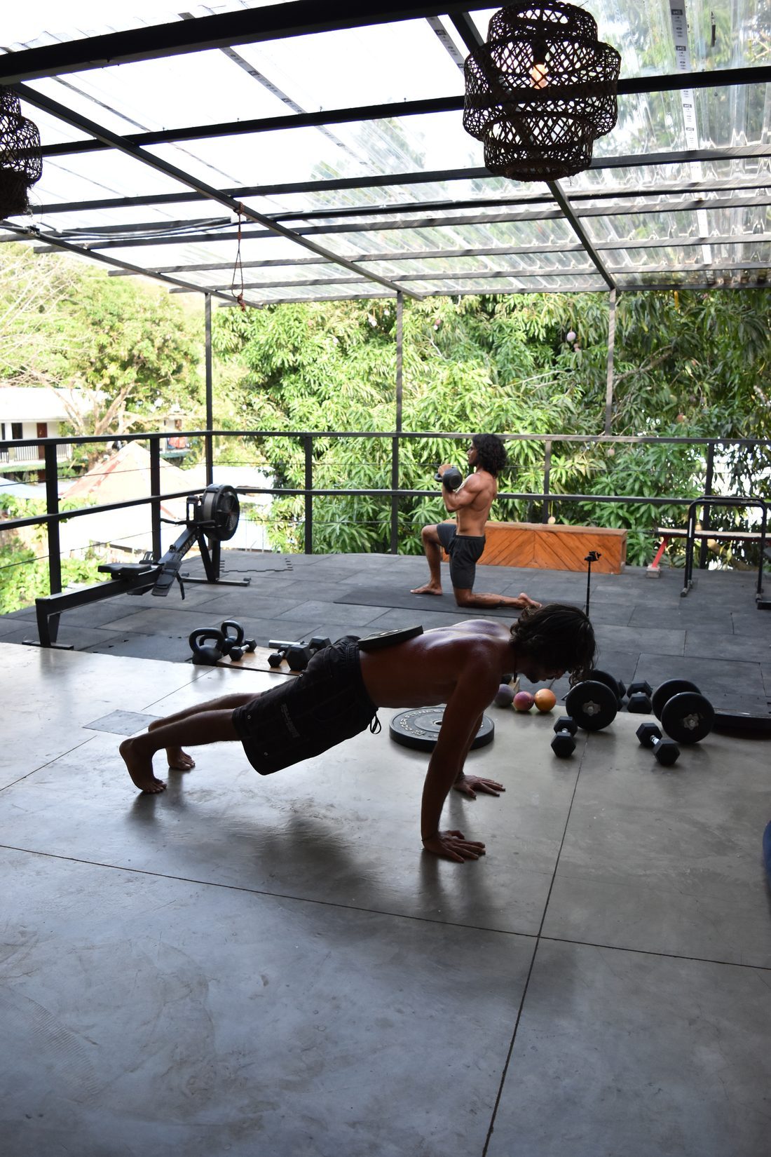Functional training on the open-air gym deck with kettlebells and a rowing machine, jungle beyond