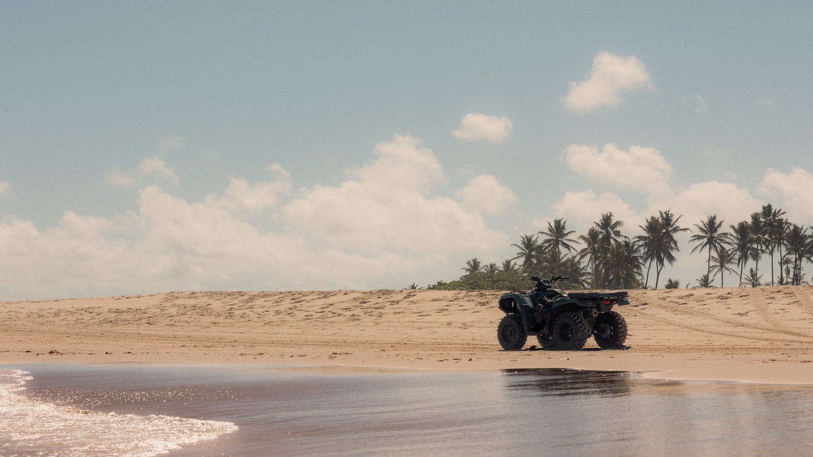 A quad bike parked on a wide tropical beach lined with palms near Santa Teresa