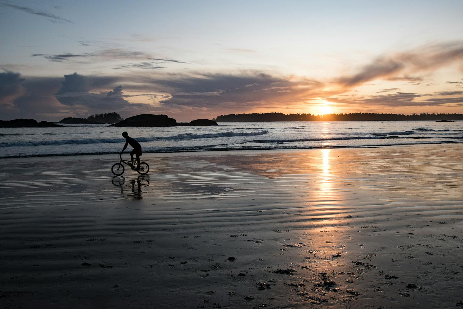 A cyclist on the wet sand at Playa Santa Teresa as the sun sets over the Pacific