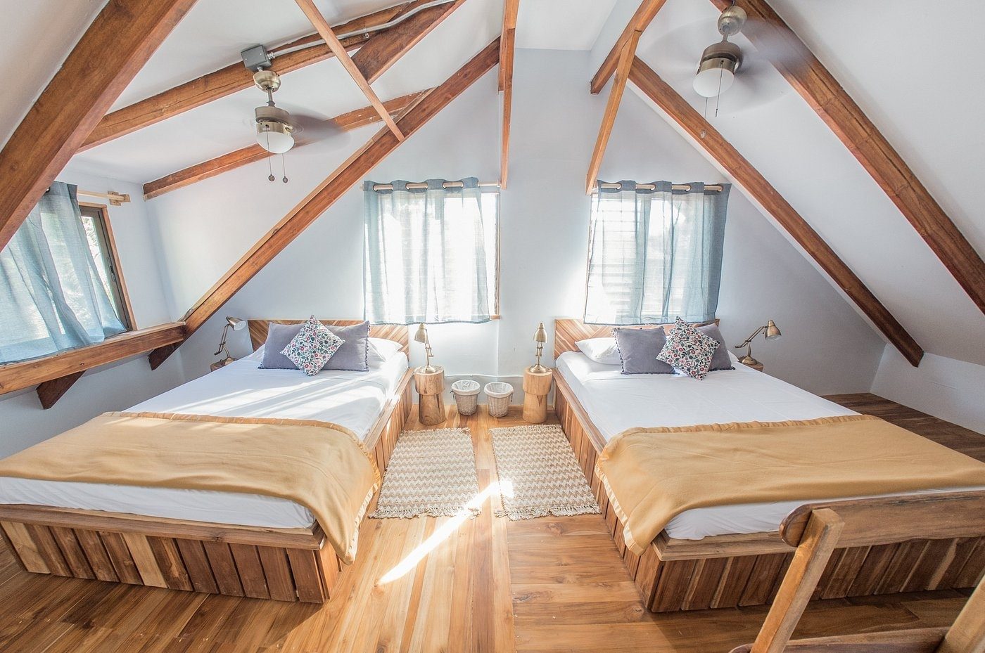 A bright A-frame room with two beds dressed in white linen and sand throws under timber beams